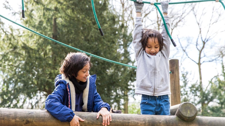 Two children climbing on a wood and rope play structure